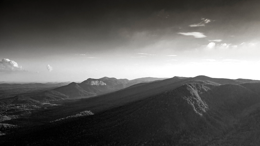 Black and white landscape of the South Carolina foothills with layered mountain ridges and soft late-day light across the valleys.