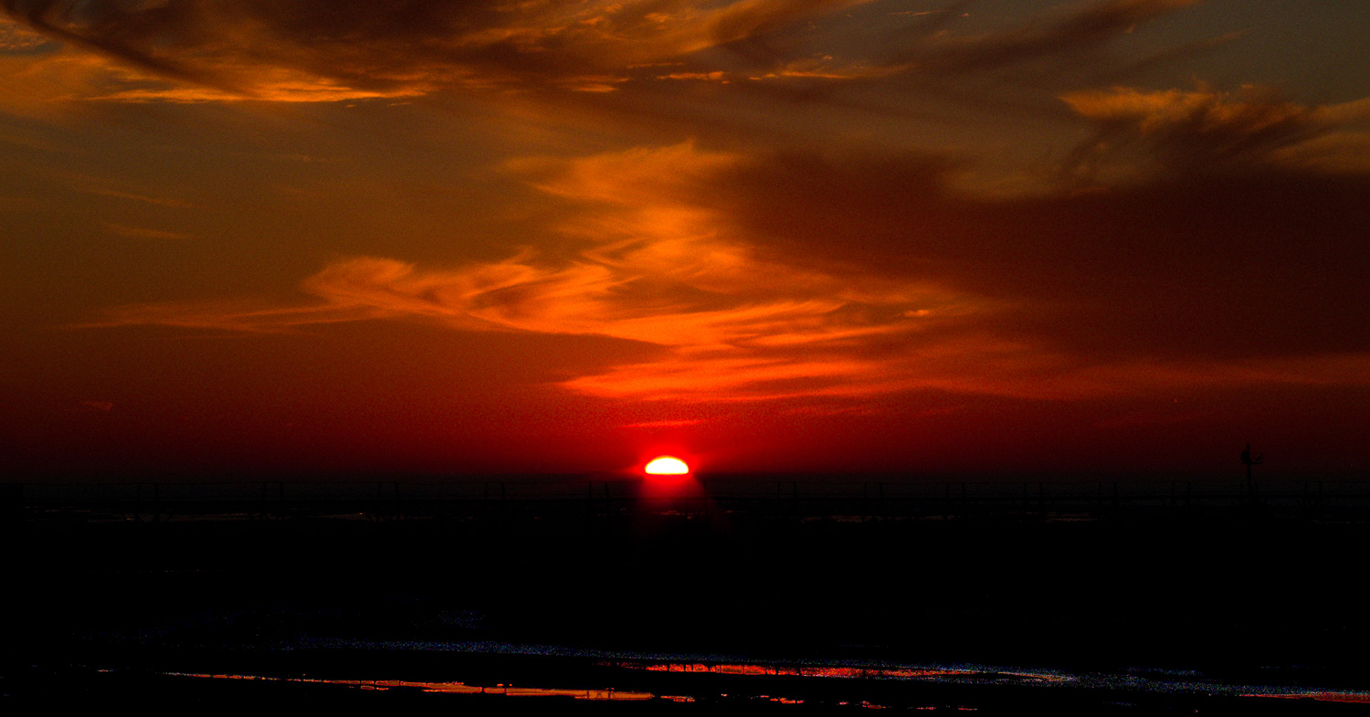 Sunset over a flat horizon with layered clouds and warm light, photographed with a minimalist landscape composition.